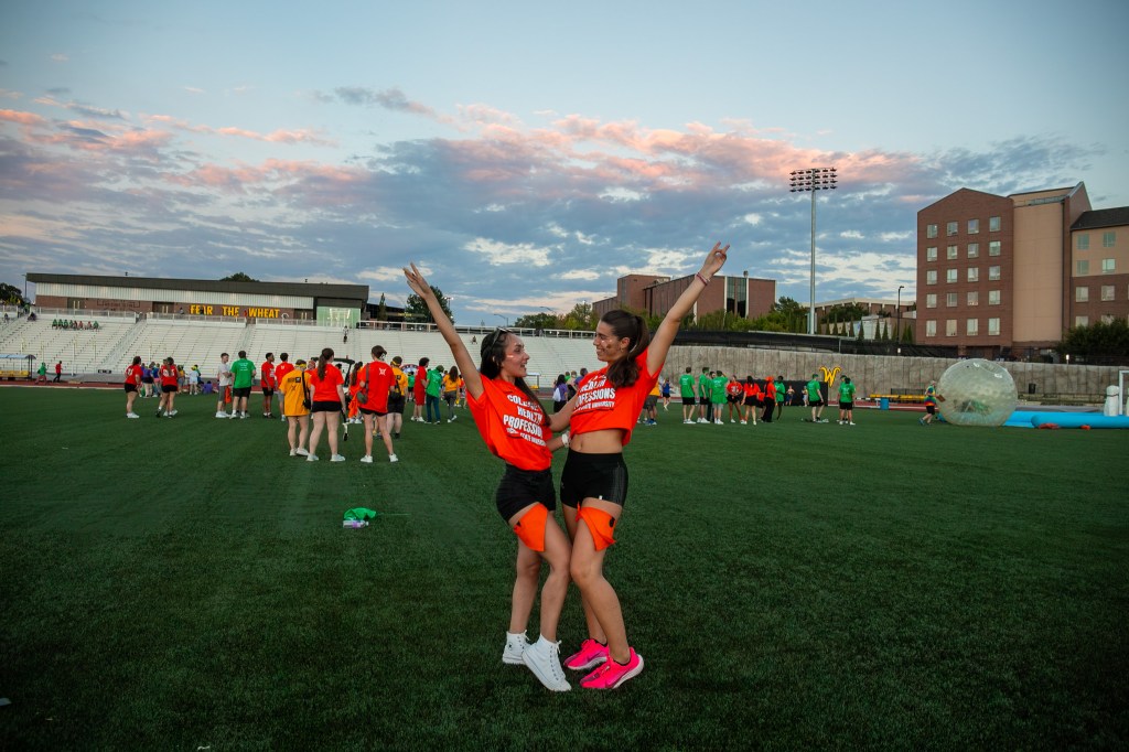 Two participants in matching red team shirts posing on a field with arms raised during a Clash of the Colleges event.