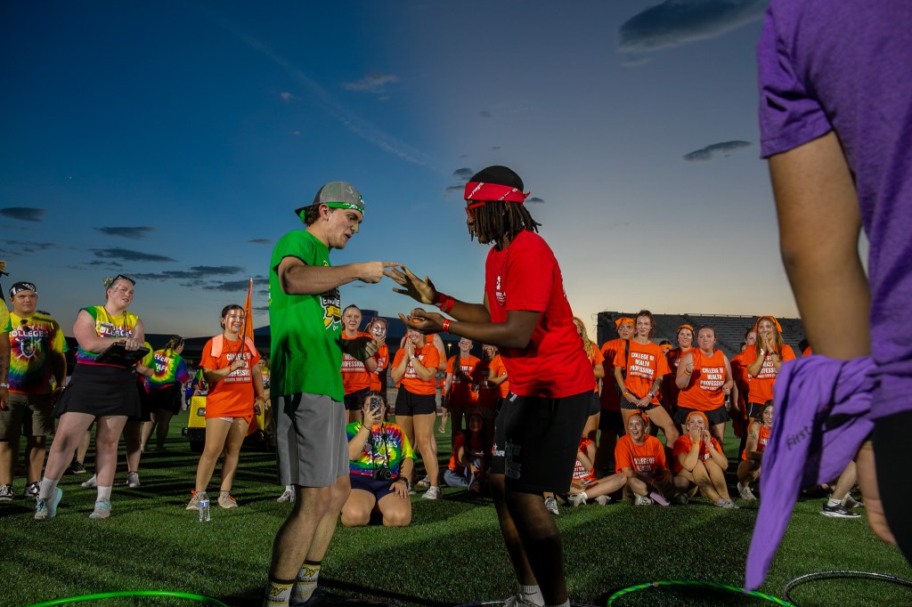 Two participants facing off in a field game while teammates and spectators watch during a Clash of the Colleges event.