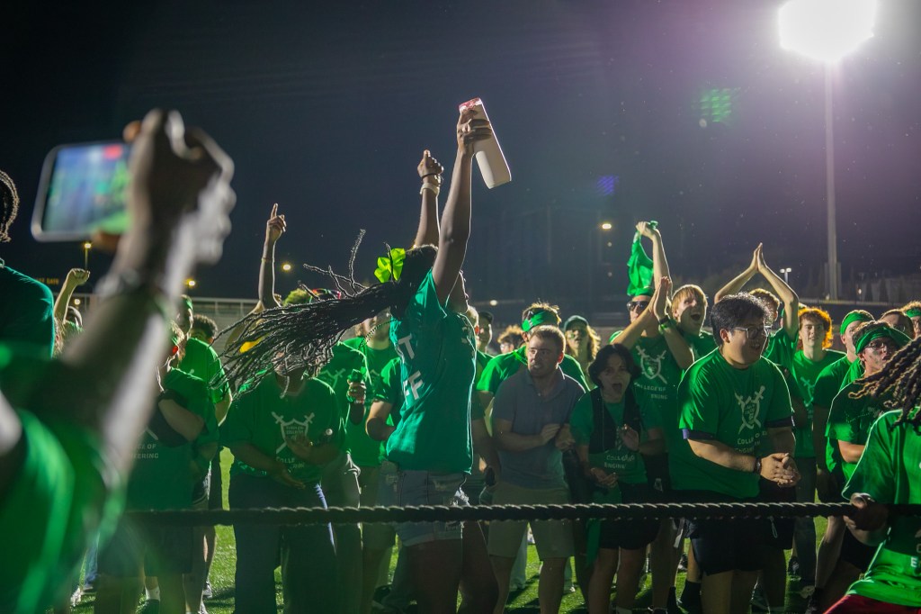 Participants in green team shirts celebrating on a field at night.
