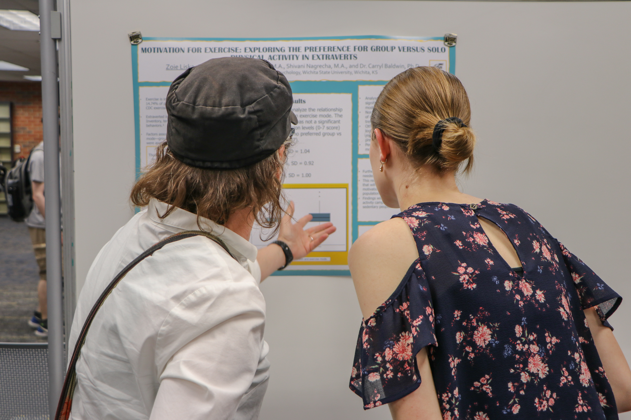 Two attendees reviewing and discussing a research poster presentation displayed on an exhibit board.