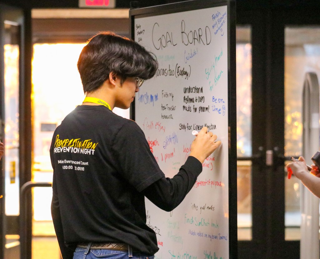 Student writing goals on a large whiteboard covered with handwritten comments and ideas.